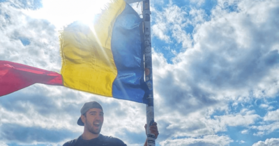 Photo of Buiuc Dragos holding a romanian flag on the top of the mountain, used in context of smrtPhone services.